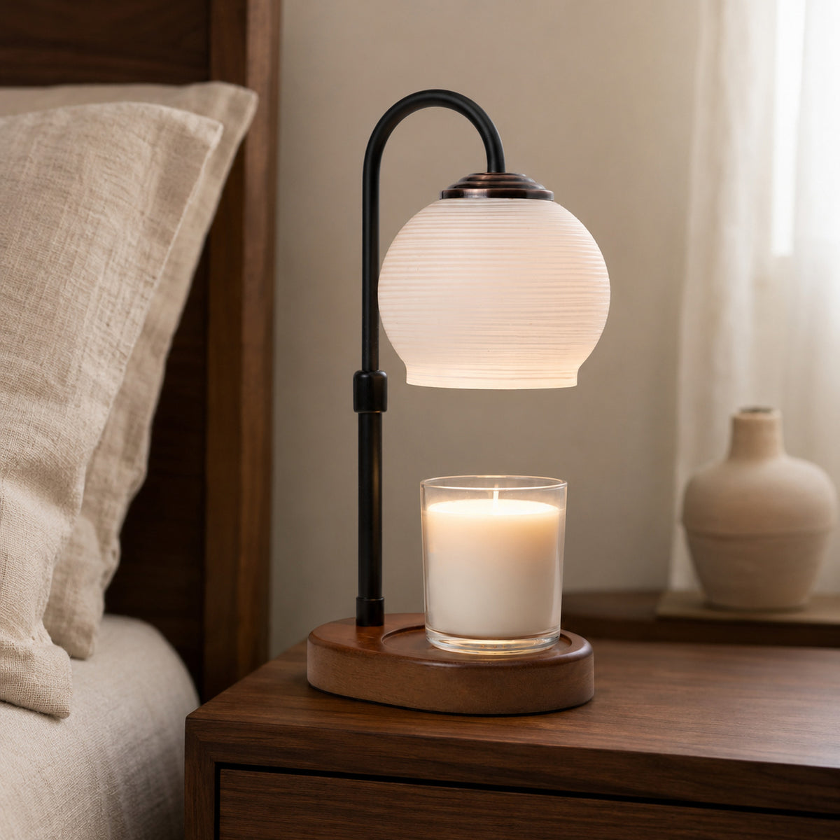 Textured Sphere candle warmer glowing over a white jar candle on a dark wooden bedside table.