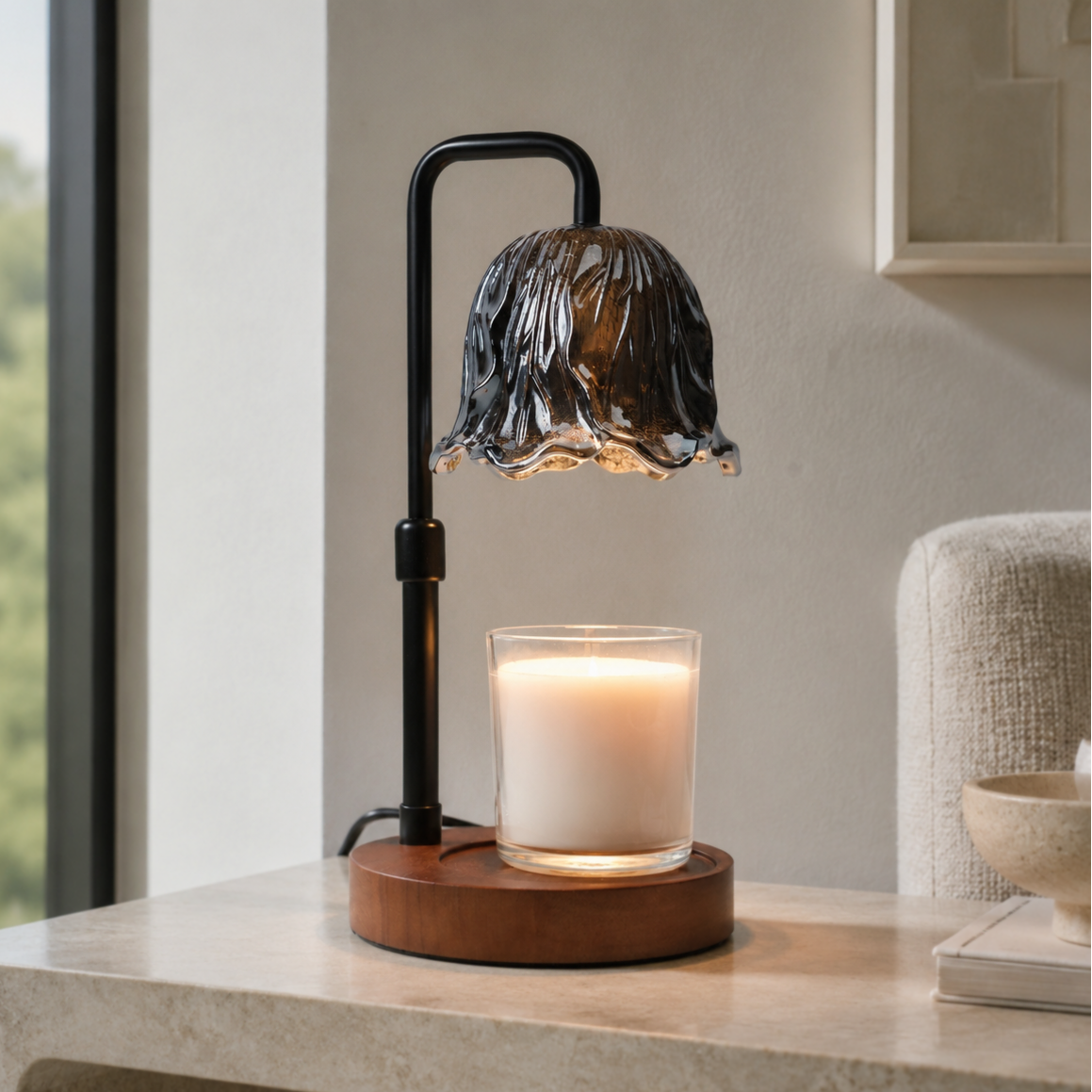 Smoked glass candle warmer lamp with a white jar candle on a pale stone table beside a window and armchair.