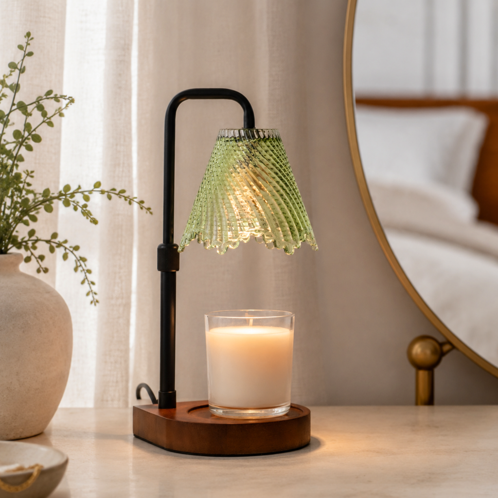 Green pleated glass candle warmer illuminated on a pale console beside a round mirror and ceramic vase.