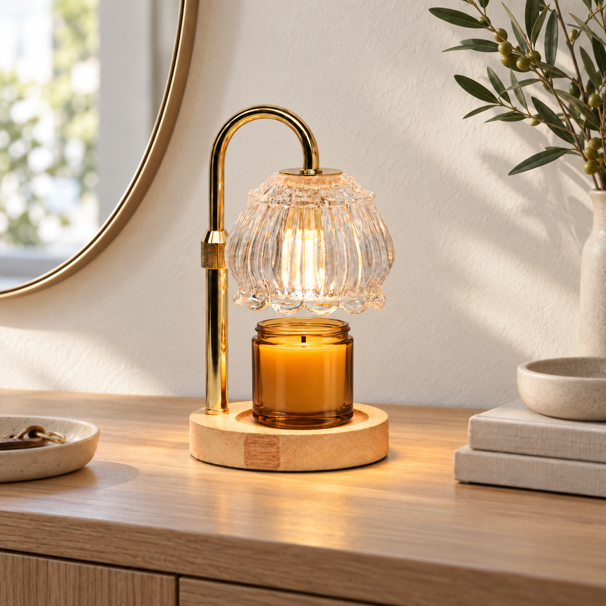 Clear glass candle warmer lamp with gold arm displayed on an entryway console beneath a mirror