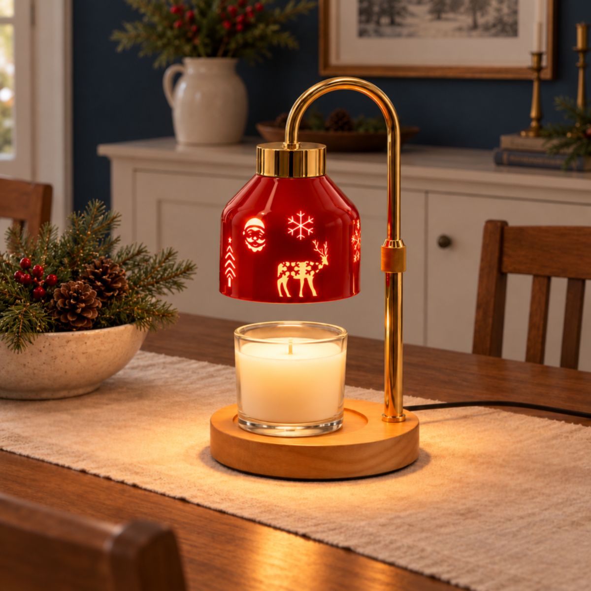 Red Christmas candle warmer lamp with a clear glass jar candle on a linen table runner beside evergreen branches and pinecones.