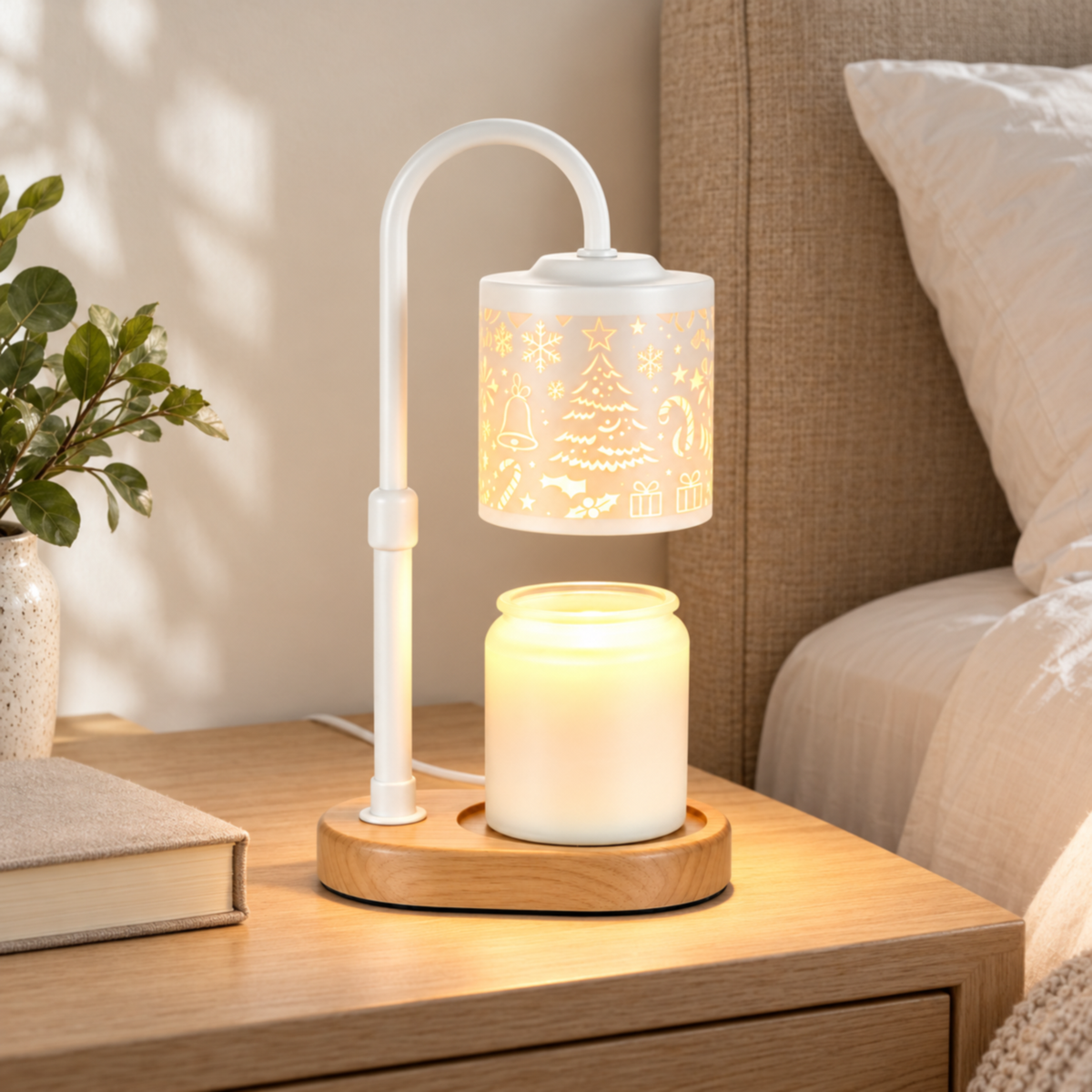 White Christmas candle warmer lamp on an oak bedside table beside ivory bedding and a linen-covered book.