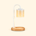 White candle warmer lamp with a glowing Christmas-patterned shade and empty wooden base on a cream background.
