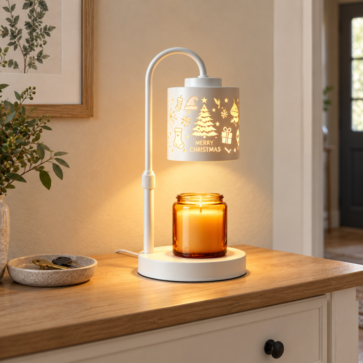 White Christmas tree patterned candle warmer lamp on an entryway console beside a ceramic key dish and botanical print.