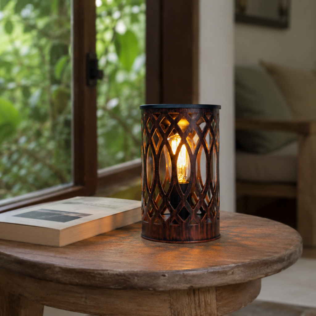 Lantern-style tabletop wax warmer glowing on a round wooden table beside an open window and book.