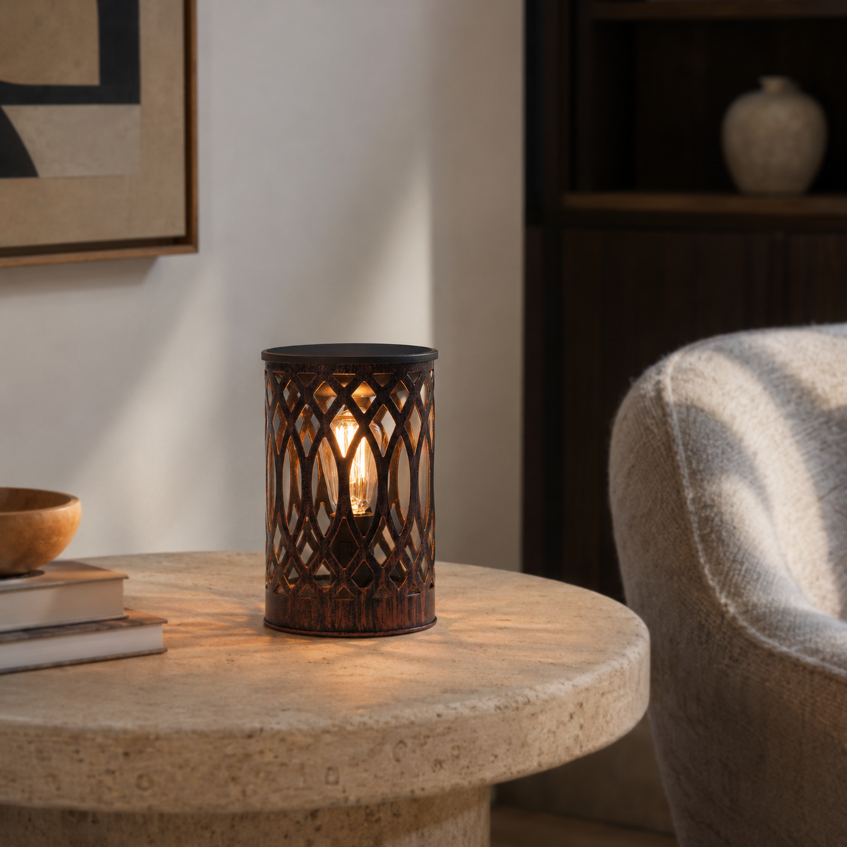 Openwork metal wax warmer illuminated on a pale stone table beside books and a cream armchair.