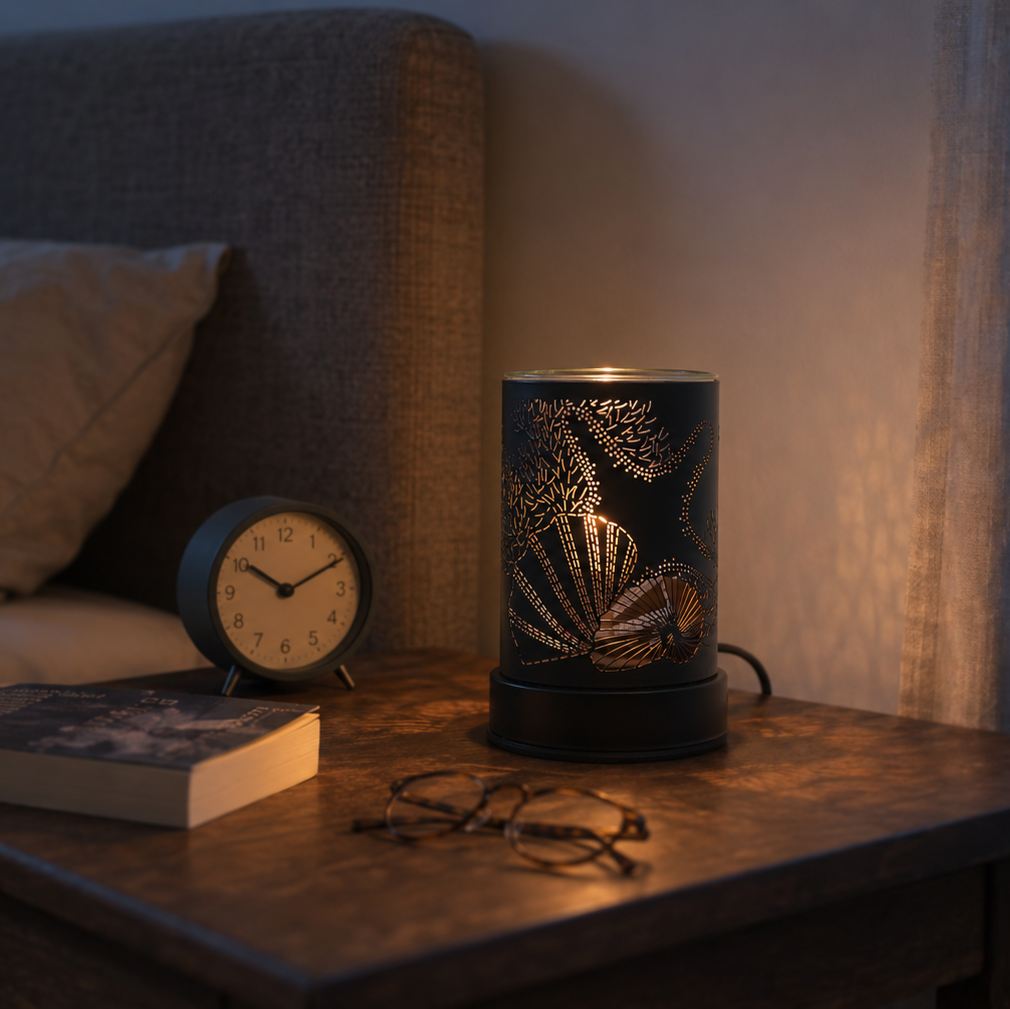 Moonlit Reef wax warmer glowing on a bedroom nightstand beside an alarm clock, book and glasses.