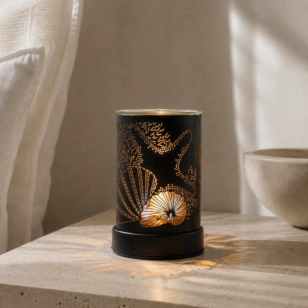 Black coastal wax warmer illuminated on a pale stone surface beside a sheer curtain and ceramic bowl.