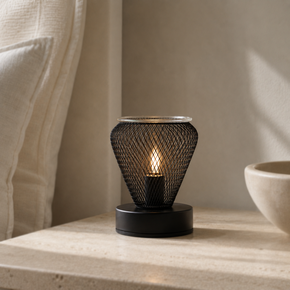 Noir Lattice Vase tabletop wax warmer glowing on a pale stone surface beside a sheer curtain and bowl.