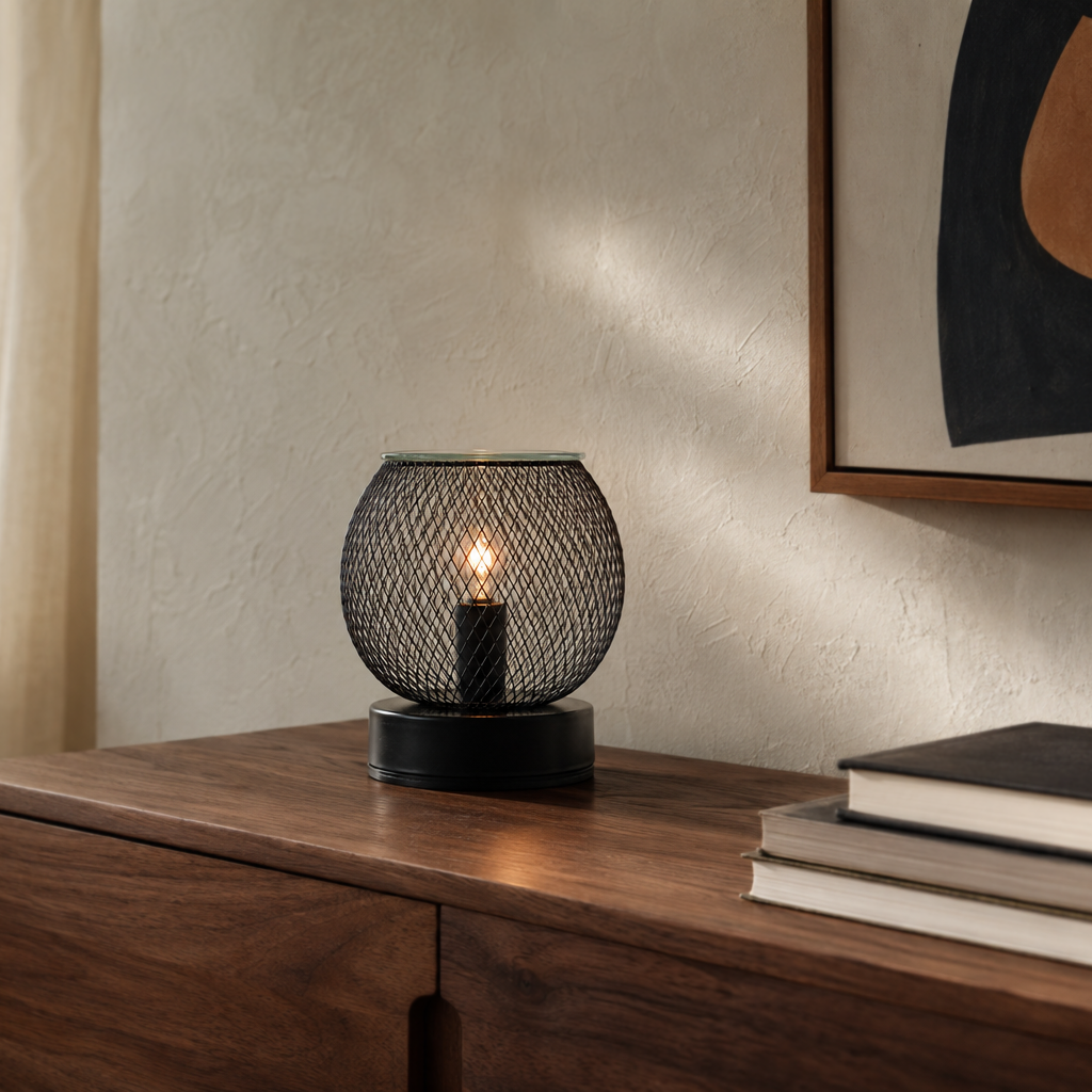 Noir Lattice Globe electric wax warmer glowing on a wooden sideboard beside books and artwork.
