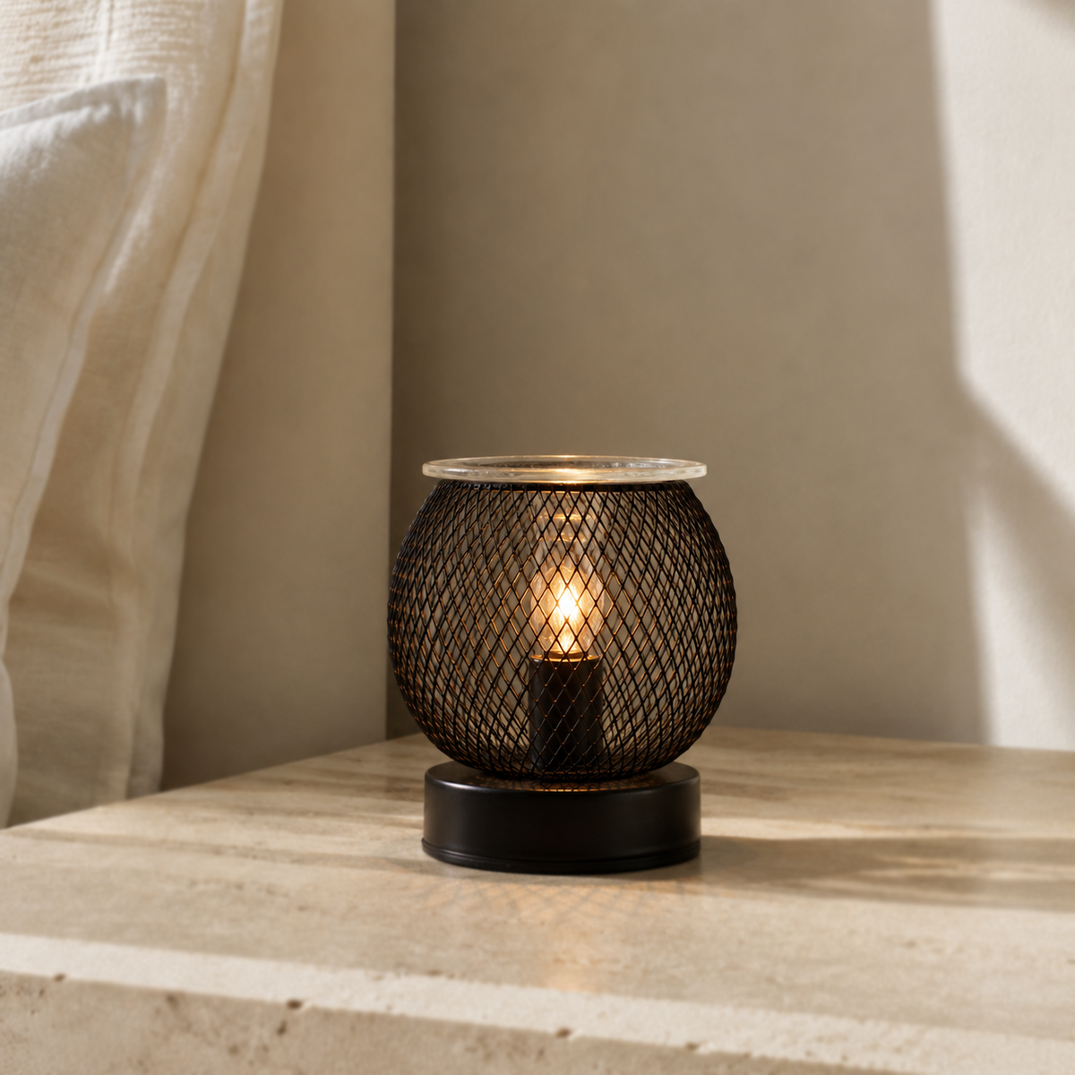 Noir Lattice Globe tabletop wax warmer glowing on a pale stone surface beside a sheer curtain.