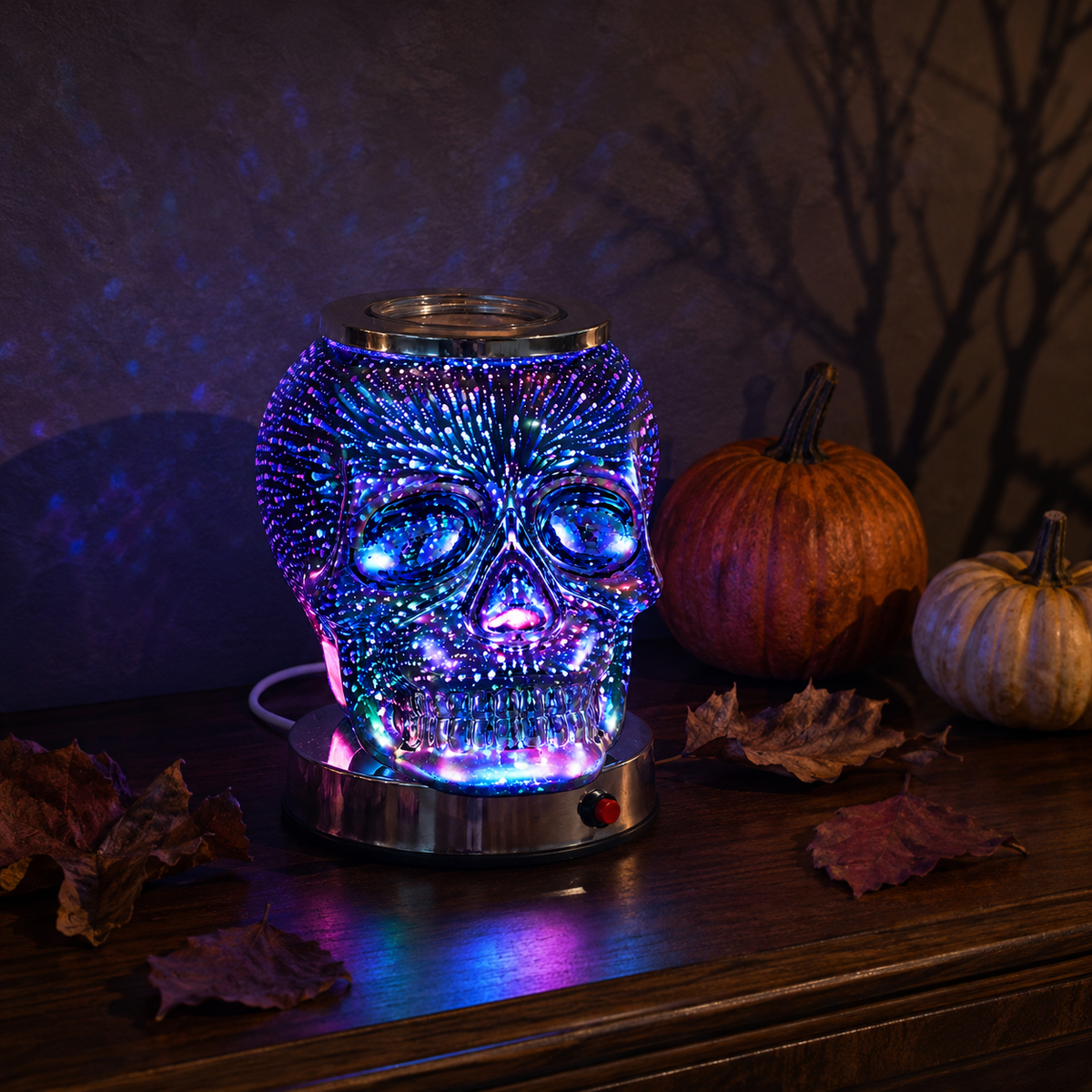 Illuminated skull wax warmer displayed with pumpkins and autumn leaves in a dark Halloween setting.