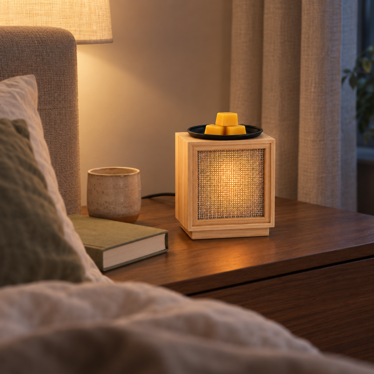 Wooden tabletop wax warmer illuminated on a bedroom nightstand beside a book and cup.