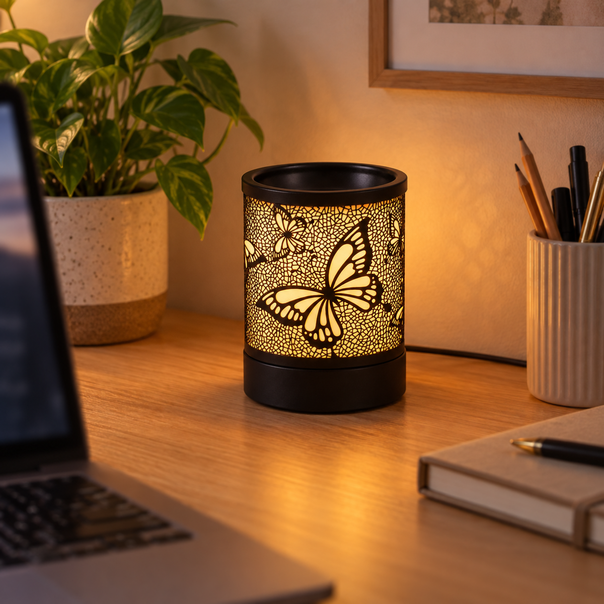 Glowing black butterfly wax warmer on a home office desk beside a laptop, notebook and plant.