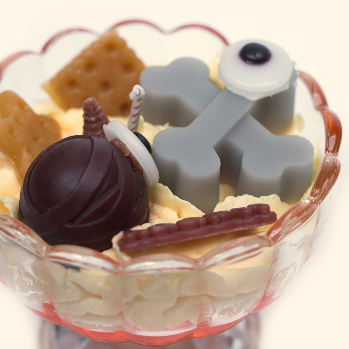 Angled close-up of the Graveyard Whispers candle with gray bones, eyeball-shaped wax pieces, dark brown spherical wax detail and assorted dessert-inspired wax pieces.