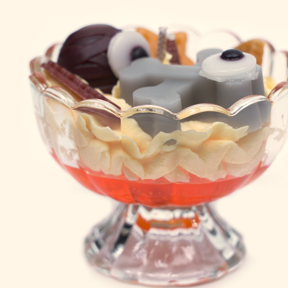 Side close-up of the sundae candle with two gray bone-shaped wax pieces, an eyeball-shaped wax piece, dark brown round wax detail and cream piped wax.