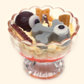 Graveyard Whispers Halloween Sundae Candle in a scalloped footed glass cup with gray bone-shaped wax pieces, eyeball details, dark brown candy pieces and cream piped wax over a red gel layer.