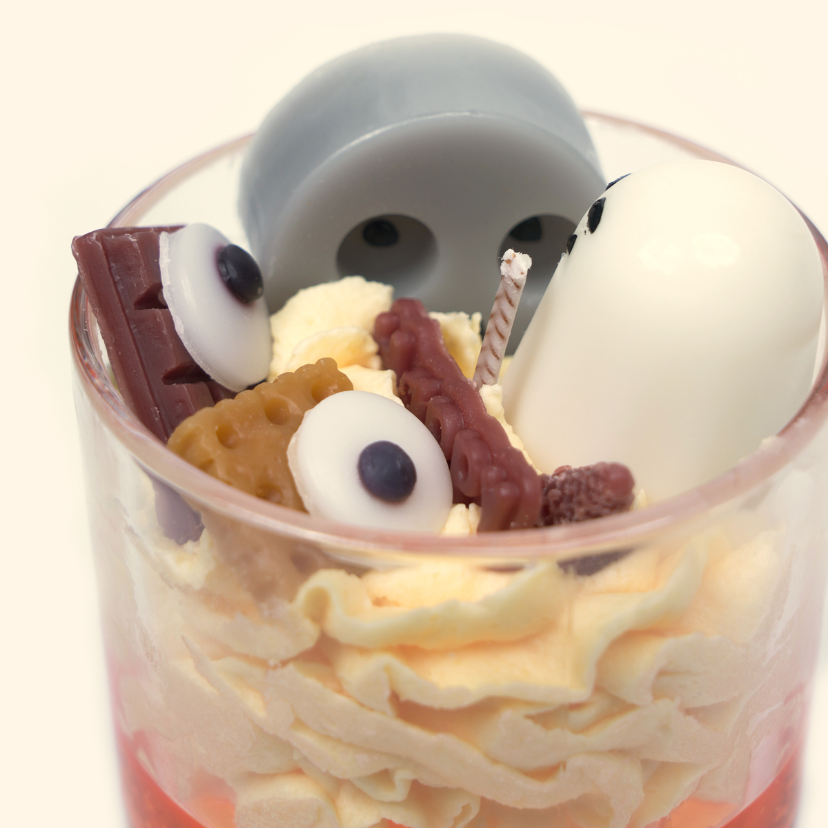 Close-up of the candle showing a large gray ghost, white ghost, eyeball-shaped wax pieces, a twisted wick and brown bar-shaped wax details.