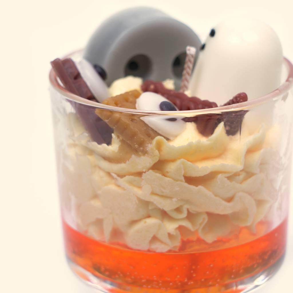 Angled close-up of the Halloween candle with gray and white ghosts, eyeball-shaped wax pieces, a twisted wick and assorted brown candy-style wax details.