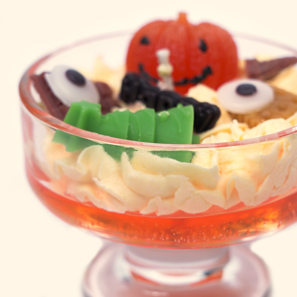 Close-up of the pumpkin candle with a green sculpted wax piece, smiling orange pumpkin, eyeball-shaped wax pieces, black wax detail and cream piped wax.