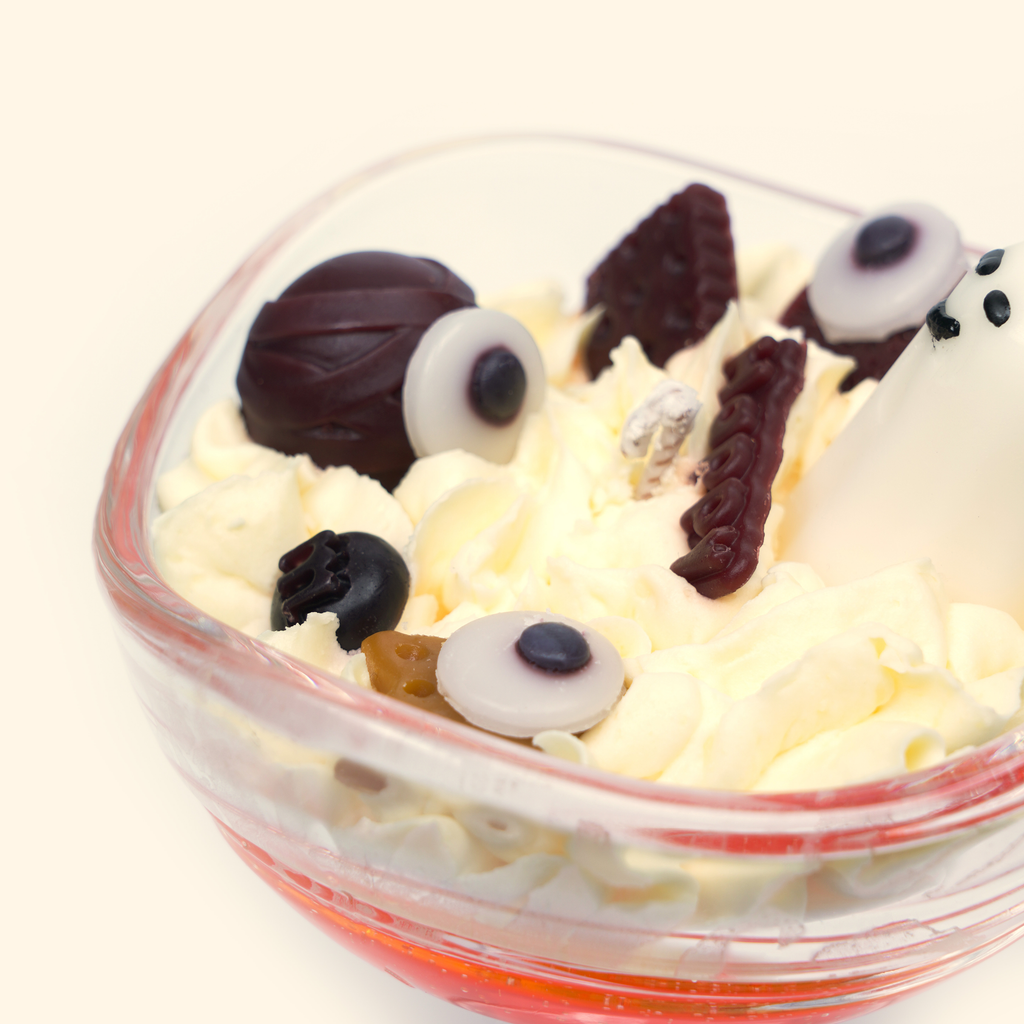 Angled close-up of the Halloween candle with a white ghost, three eyeball-shaped wax pieces, a twisted wick and dark brown bar-shaped wax details.
