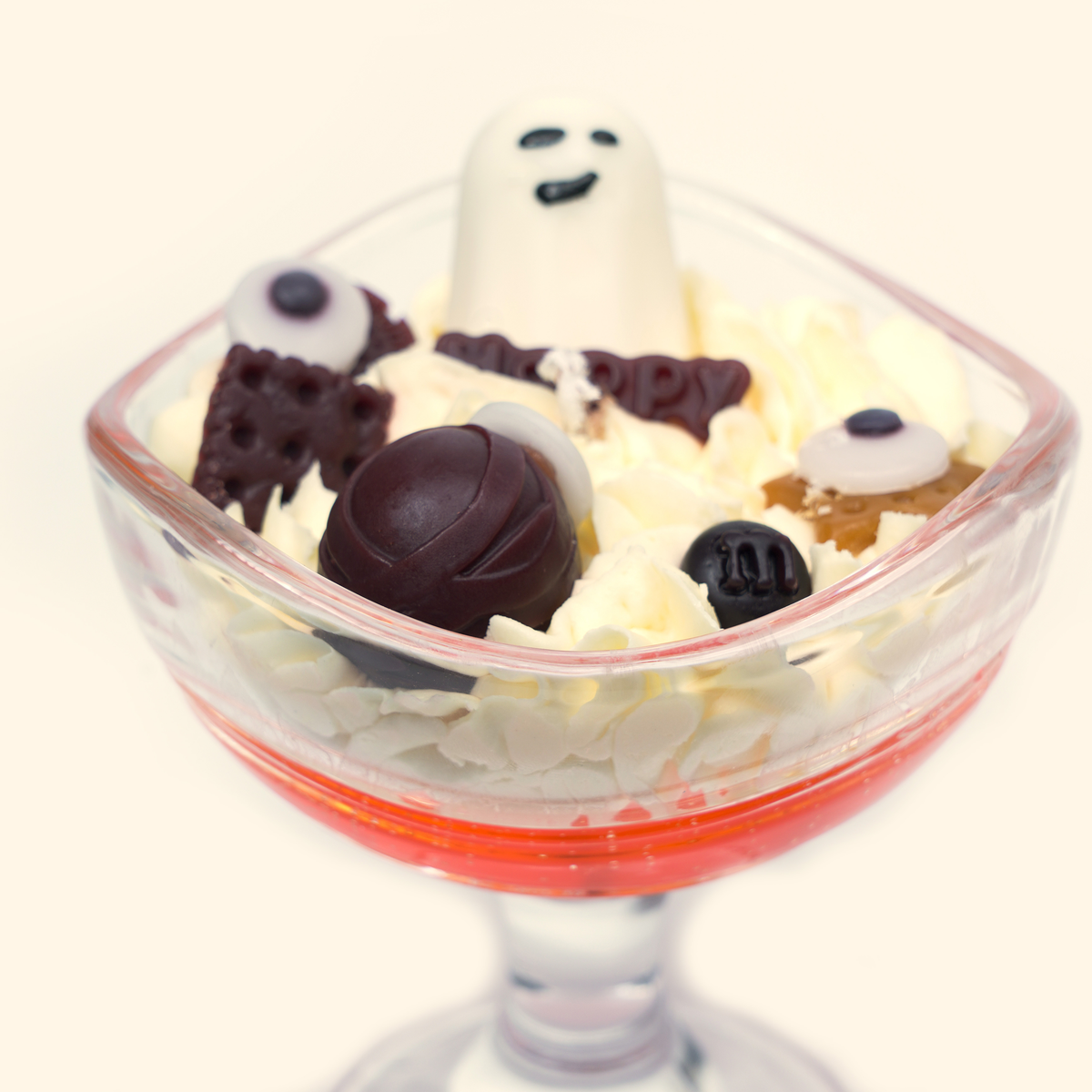 Close front view of the ghost candle with a smiling white ghost, eyeball-shaped wax pieces, a dark brown round wax piece and a Happy plaque among cream piped wax.