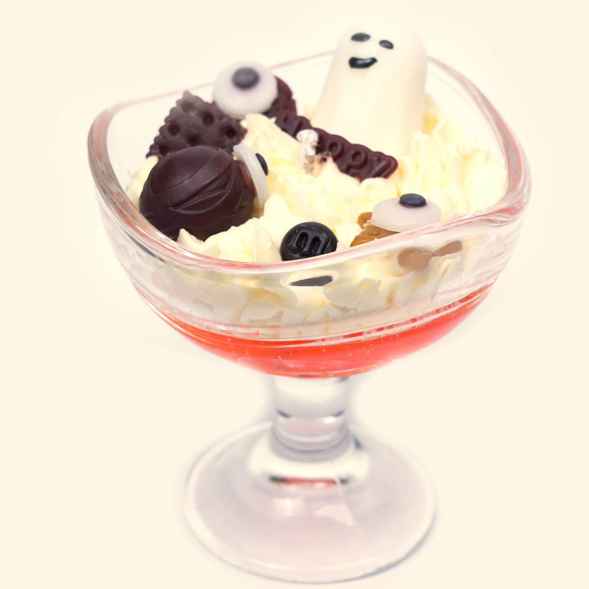 Ghost Candy House Halloween Candle in a scalloped footed glass cup with a white ghost, eyeball-shaped wax pieces, dark brown candy details and cream piped wax over a red gel layer.