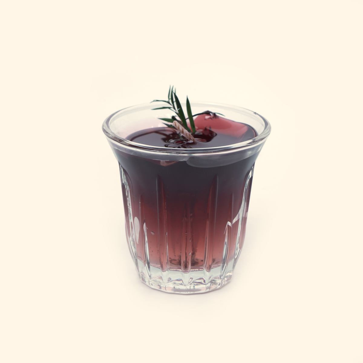Iced Americano Coffee Candle with dark translucent coffee-colored wax, a twisted wick, green needle-like sprig and ice-cube details in a clear fluted glass cup.