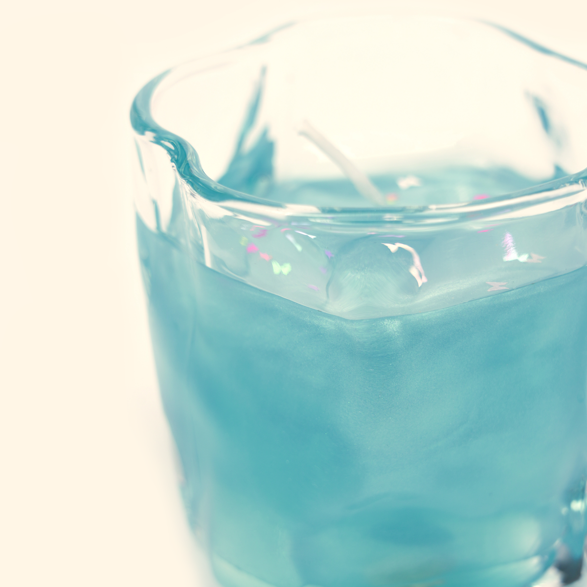 Close-up of the Ocean Dream candle showing shimmering blue gel wax, colorful confetti and the curved rim of the clear glass cup.