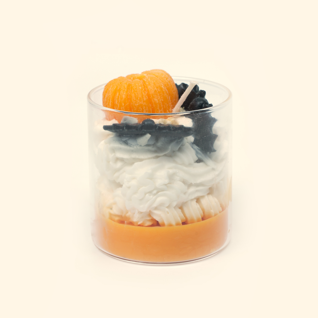 Front view of the Halloween candle with a sculpted orange pumpkin, black bat decorations, cream-colored wax swirls and an orange wax base.