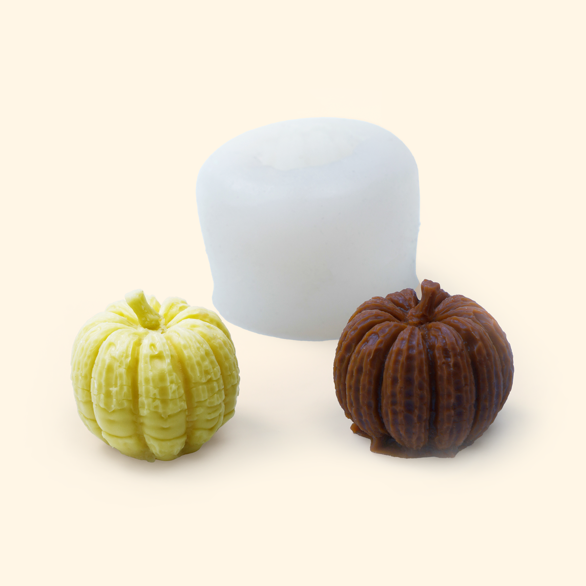 Translucent small pumpkin silicone mold displayed beside sample finished wax pieces showing the sculpted pumpkin shape.