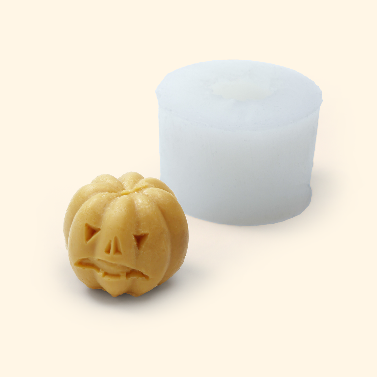 Translucent silicone pumpkin mold displayed beside a sample finished wax piece showing the smiling jack-o’-lantern shape.