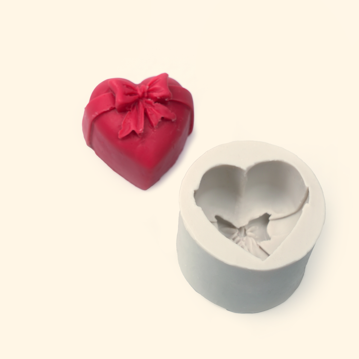 Heart-shaped silicone mold displayed beside a sample finished wax piece showing the sculpted bow design.