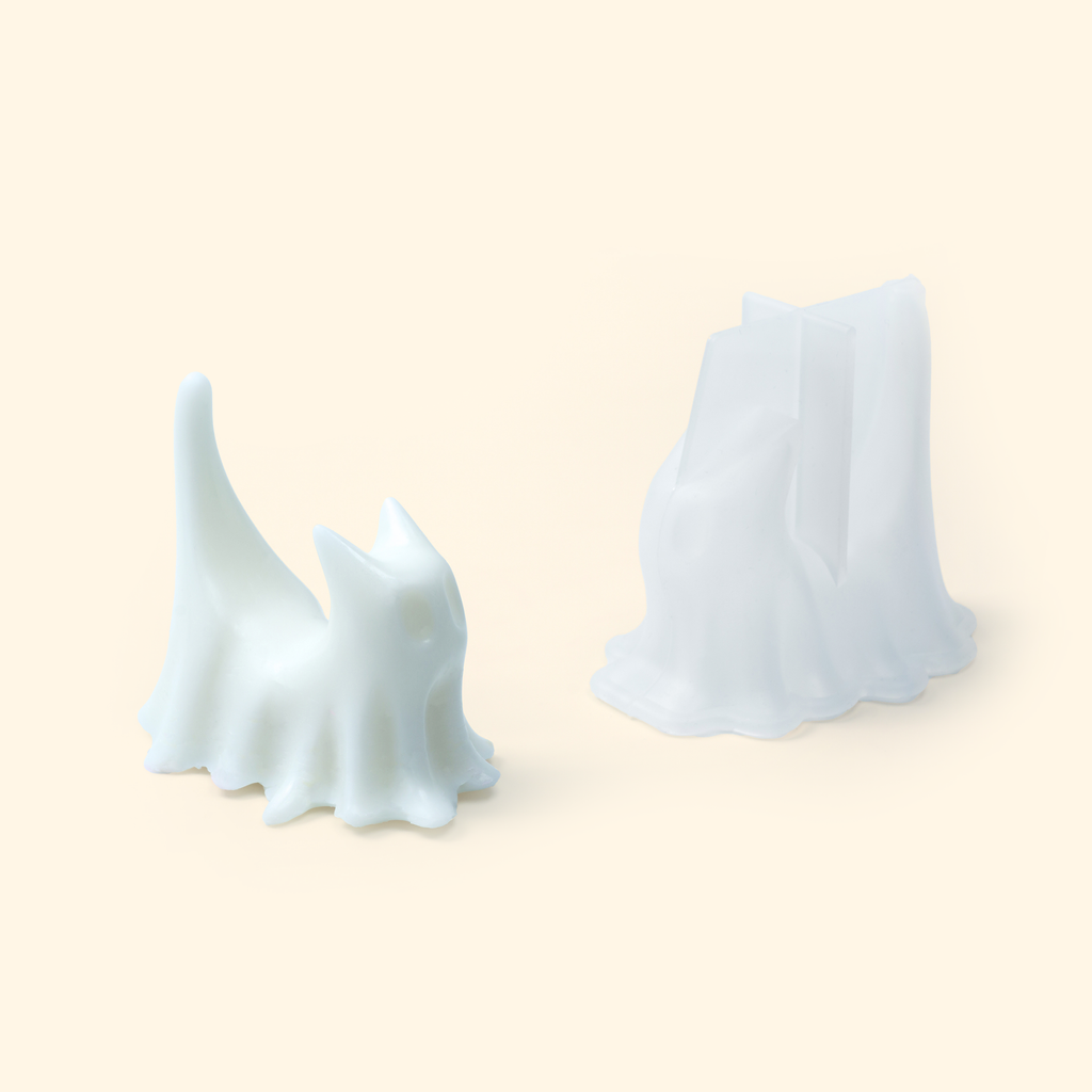 Translucent silicone ghost cat mold displayed beside a sample finished wax piece showing the sculpted tail and draped details.