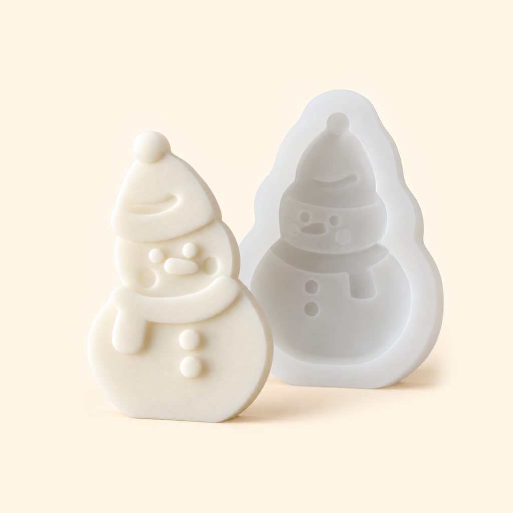 White snowman silicone mold with an open cavity beside an ivory casting wearing a hat and scarf.