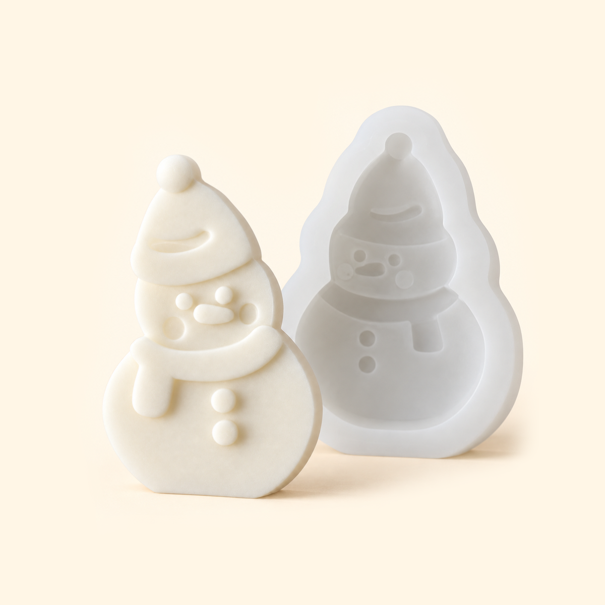 White snowman silicone mold with an open cavity beside an ivory casting wearing a hat and scarf.