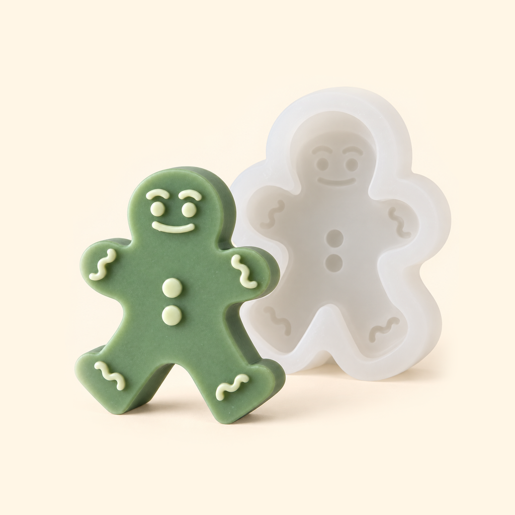 White gingerbread man silicone mold beside a sage green casting with ivory facial details and decorative trim.
