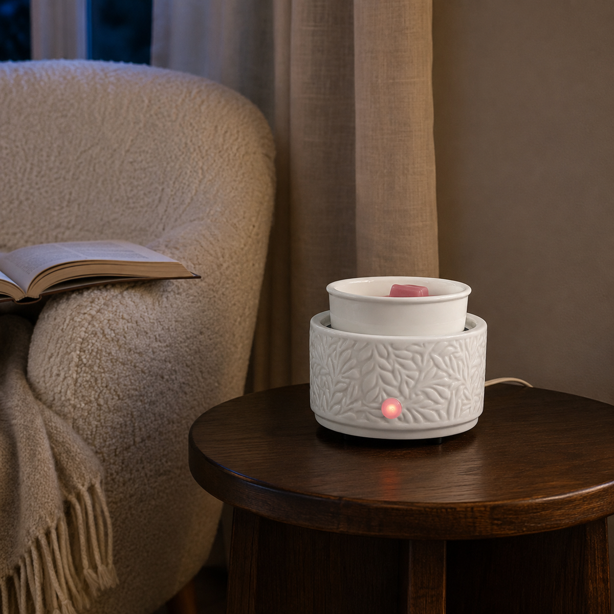 Ivory ceramic wax warmer with illuminated control indicator on a dark side table beside a boucle chair.